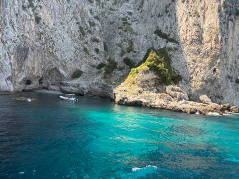 Rocky Capri coastline with turquoise water and a small motorboat exploring nearby caves