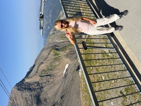 Girl giving a peace sign at a mountain viewpoint with rocky peak and cable in background