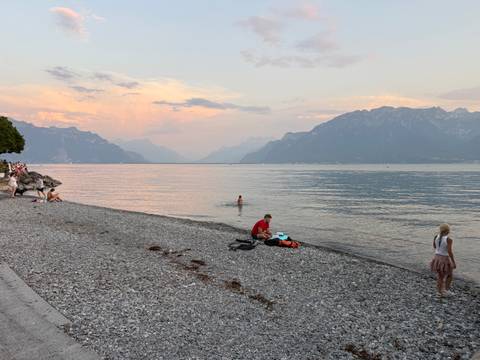 Pebble beach on Lake Geneva at dusk with swimmers and families enjoying the calm water