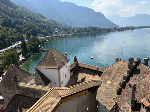 Panoramic view from Chillon Castle rooftops across Lake Geneva with mountains and swimmers below