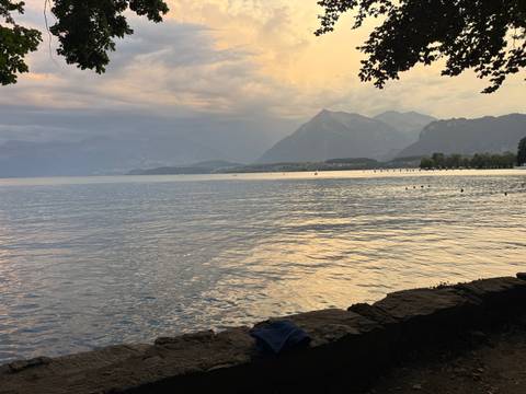 Soft evening light over a calm lake with mountain silhouettes and moody clouds