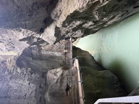 Person standing on a suspended walkway inside a dramatic narrow gorge with turquoise water below