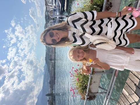 Mother and daughter enjoying ice cream on a lakeside pier with mountains and bright sky
