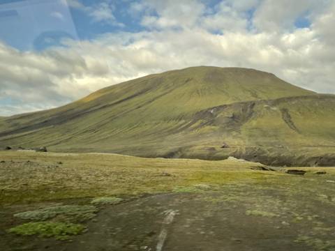 Motion-blurred foreground of barren Icelandic plateau with a smooth-sloped mountain in cloudy light.
