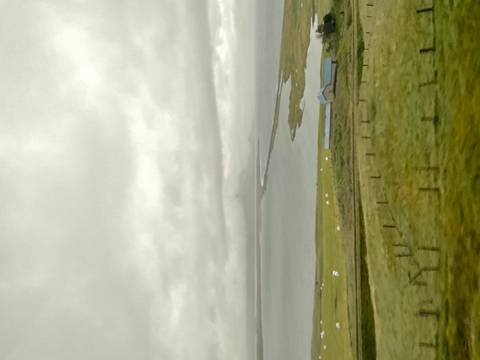 Vertical blurry shot of Icelandic coastline with distant low mountain under grey skies.