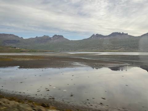 Tidal flats reflecting rugged mountains under overcast skies in East Iceland.