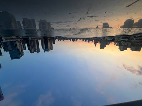 Modern skyscrapers rise along a river at sunset with boats moored in the fading golden light.