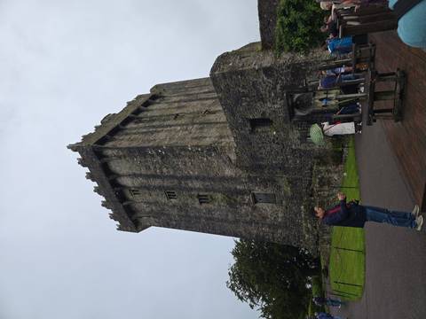 Visitors gather near the towering stone walls of historic Blarney Castle on a cloudy day.
