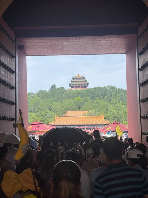 Crowds exit a palace gate framing the hilltop Wanchun Pavilion in Beijing's Forbidden City.
