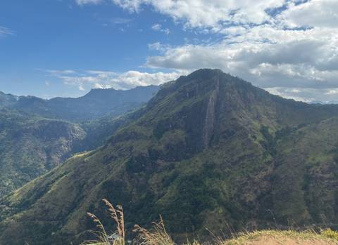 Lush green Sri Lankan mountain ridge under a partly cloudy sky with deep valleys below.