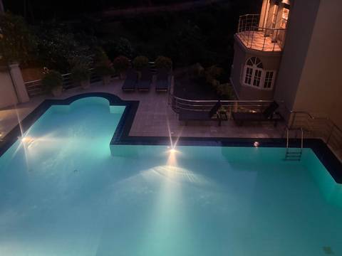Night view of a hotel swimming pool softly lit with blue underwater lights and loungers nearby.