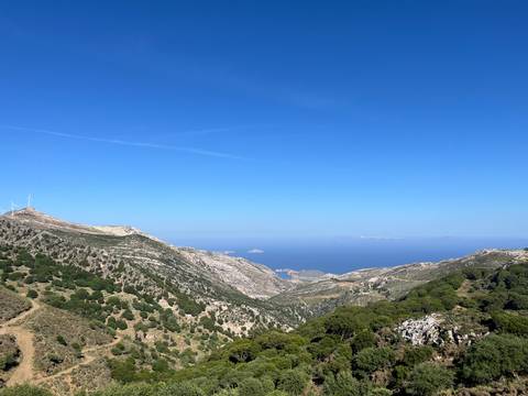 Expansive mountain ridge descending to the deep blue Aegean Sea under clear sky.