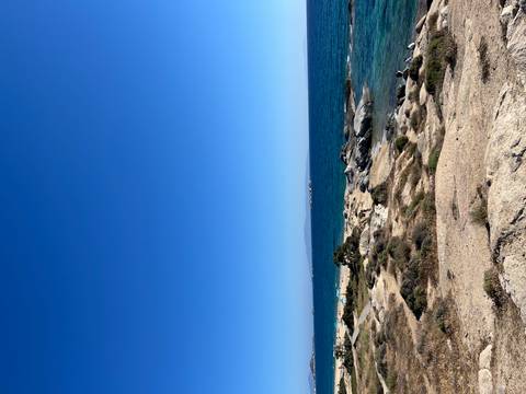 Rocky seaside landscape with clear Aegean water and visitors scattered along the shore.