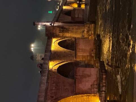 Historic Stone Bridge spanning river, softly lit with reflections in water on a misty night.