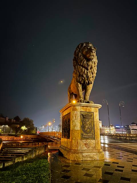 Majestic stone lion statue on pedestal illuminated against dark night sky.