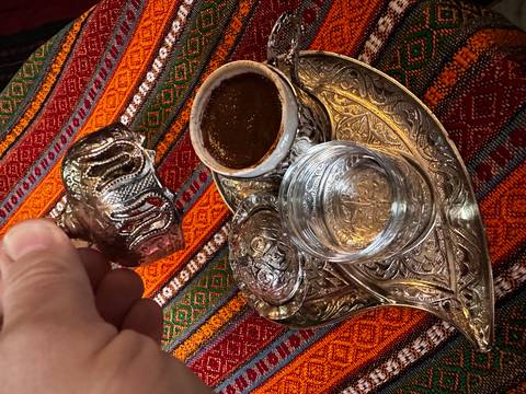 Close-up of traditional Balkan coffee set with ornate metalwork on colourful woven tablecloth.