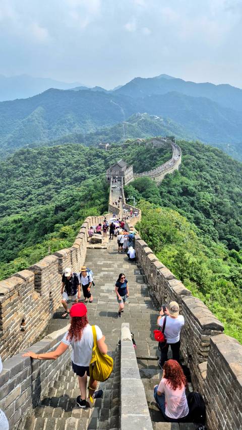 Busy section of the Great Wall of China snaking across green mountains filled with tourists.
