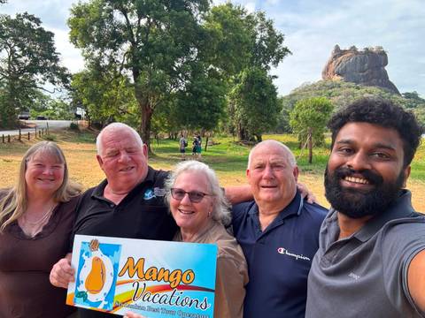Group selfie holding tour sign with Sigiriya Rock fortress rising in the background
