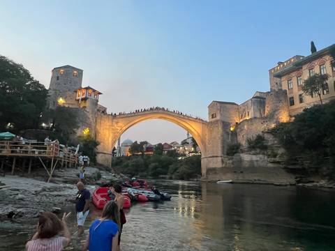 Early evening view of Stari Most bridge with people on rafts and warm lights beginning to glow