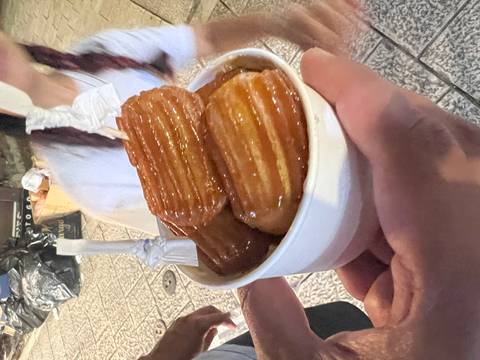 Cup filled with syrup-coated churro desserts held in someone’s hand at night market