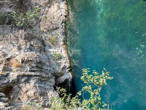 Clear turquoise spring emerging from a cave mouth in a limestone cliff