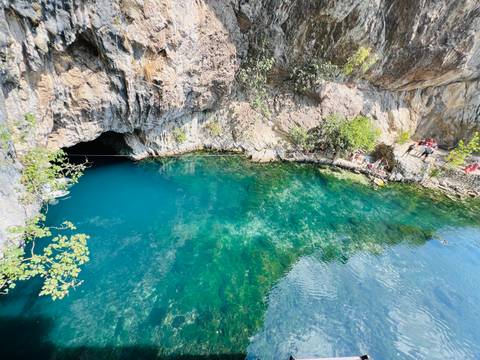 Wide view of the emerald Buna Spring pool with visitors standing on rocks near the water