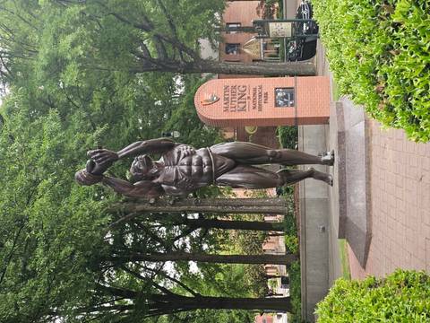 Muscular bronze statue holding a baby beside a Martin Luther King Jr. National Historical Park brick sign surrounded by trees