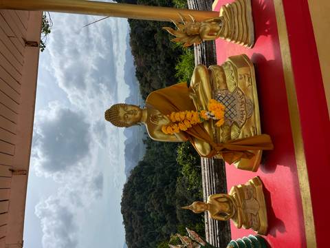 Gold Buddha statues on a red altar overlooking lush jungle hills and dramatic limestone peaks