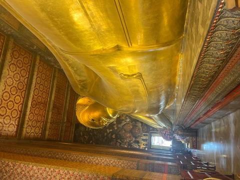 Golden Reclining Buddha statue inside Wat Pho temple with ornate patterned ceiling
