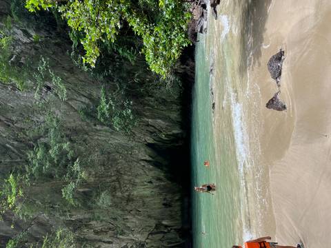 Secluded cove with turquoise water, karst cliff backdrop and two bathers enjoying the shallow waves