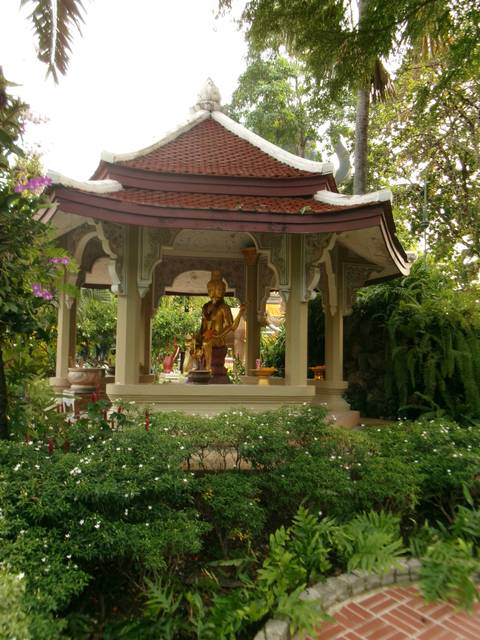 Small open pavilion housing a golden deity statue within a lush tropical garden