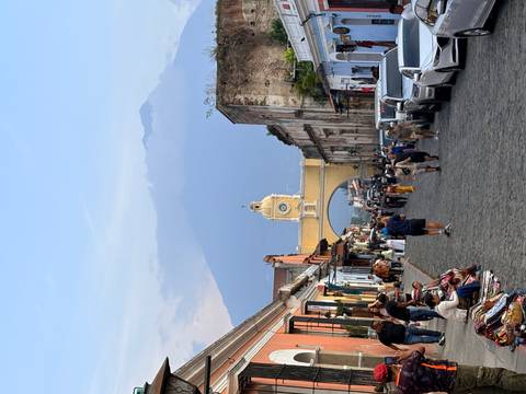 Cobblestone street of Antigua leads to the iconic yellow Santa Catalina Arch with looming volcano backdrop and bustling vendors.