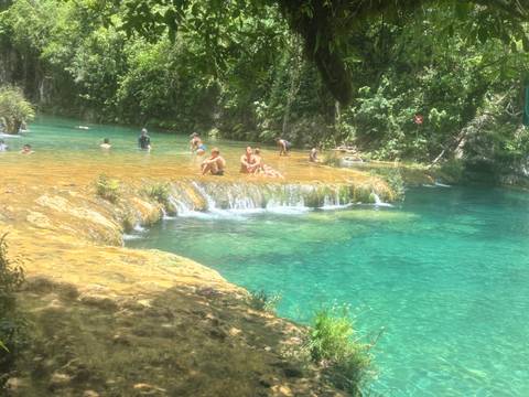 Visitors swim and relax in vivid turquoise tiered pools surrounded by lush jungle foliage.
