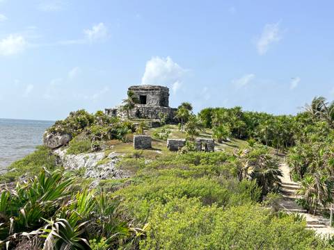 Stone Mayan ruin perched atop a coastal cliff surrounded by jungle with the Caribbean Sea below.