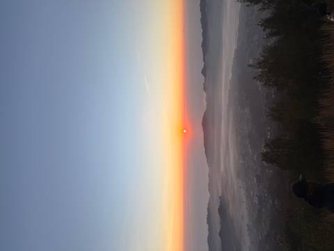 Orange sun rises above mist-filled valley and layered volcanic peaks under a clear gradient sky.