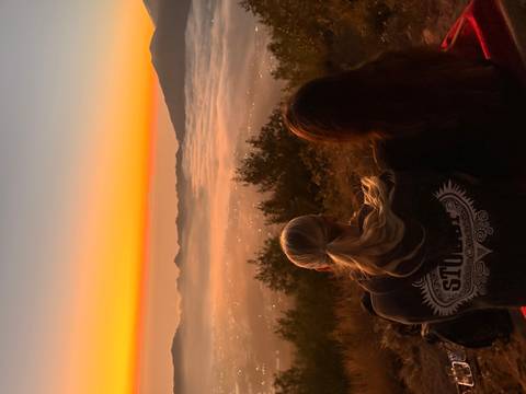 Couple sits together watching a vivid sunrise over cloud-blanketed valley and mountain ridge.