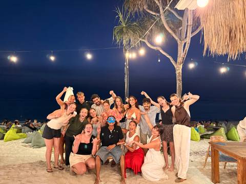 Cheerful group raises fists for a night photo at a beach bar lit by string lights.