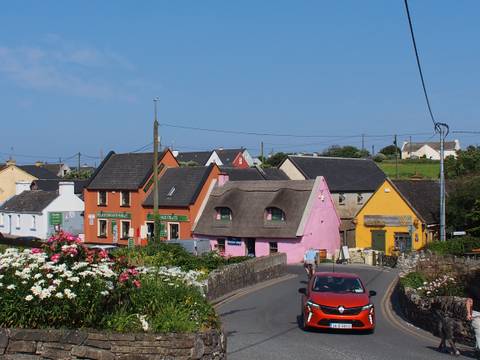colorful Irish village with thatched pink cottage, orange and yellow shops and summer flowers