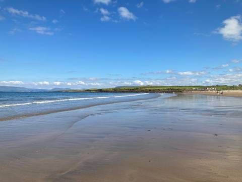wide sandy beach with gentle waves and distant headlands under a bright blue sky