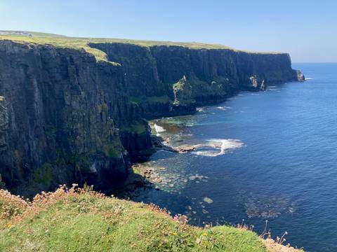 towering dark cliffs dropping into deep blue Atlantic waters with patches of turquoise