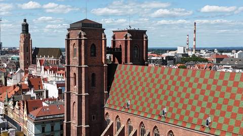 close aerial of a brick church with patterned tiled roof and city skyline of Wroclaw