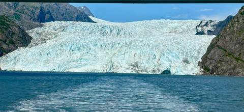 Huge tidewater glacier meeting the turquoise sea with boat wake in the foreground on a bright day