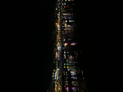 Row of colorful paper lanterns reflecting on a river at night in a lively market town