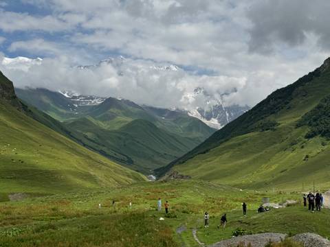 Verdant Georgian valley framed by steep mountains and distant snow peaks partly veiled by clouds