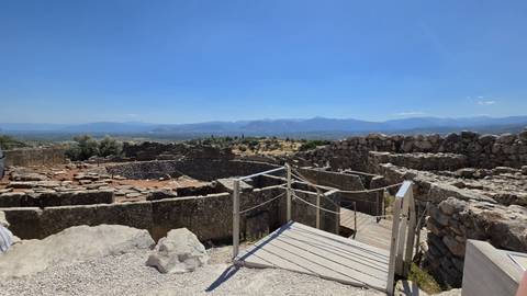 Stone walls and a circular grave complex overlook a valley and distant mountains at an archaeological site.