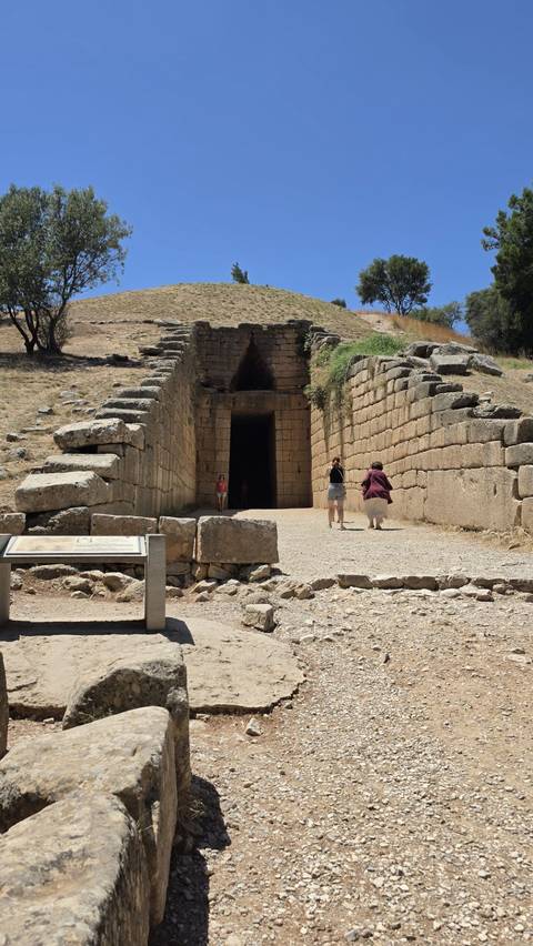 Visitors stand at the massive stone entrance of the beehive-shaped Treasury of Atreus tomb.