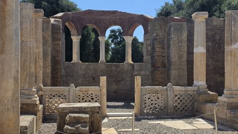 Remains of an early Christian basilica with ornate arches and stone latticework bathed in sunlight.
