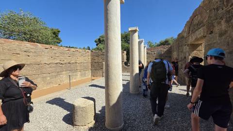 Tourists walk between marble columns and ancient walls inside an archaeological site.