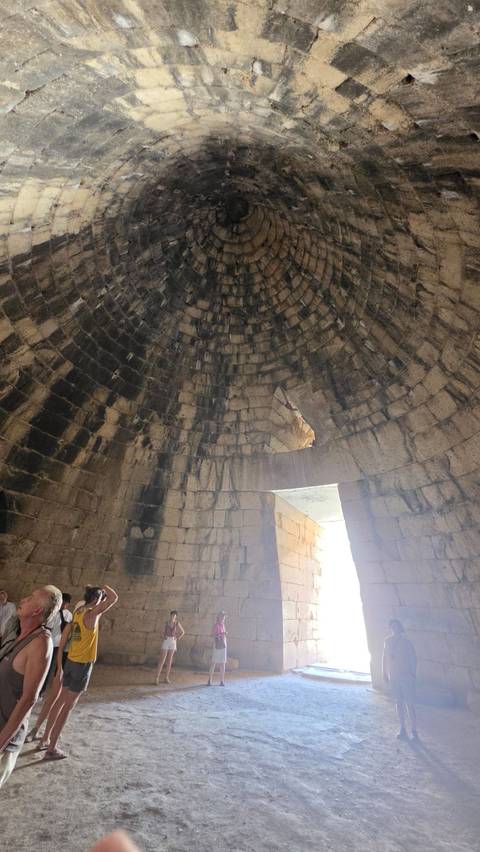 Stone-lined, corbelled dome interior of an ancient tholos tomb with light filtering through the doorway.