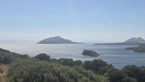 Peaceful coastal view of blue waters dotted with small islands beyond green hills.